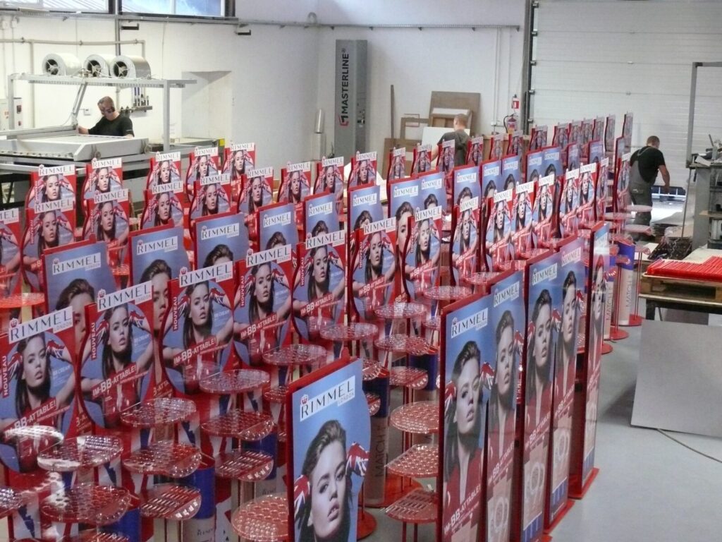 Produkcja standów reklamowych w zakładzie zajmującym się materiałami POS, z widokiem na rzędy gotowych ekspozytorów. - Opole